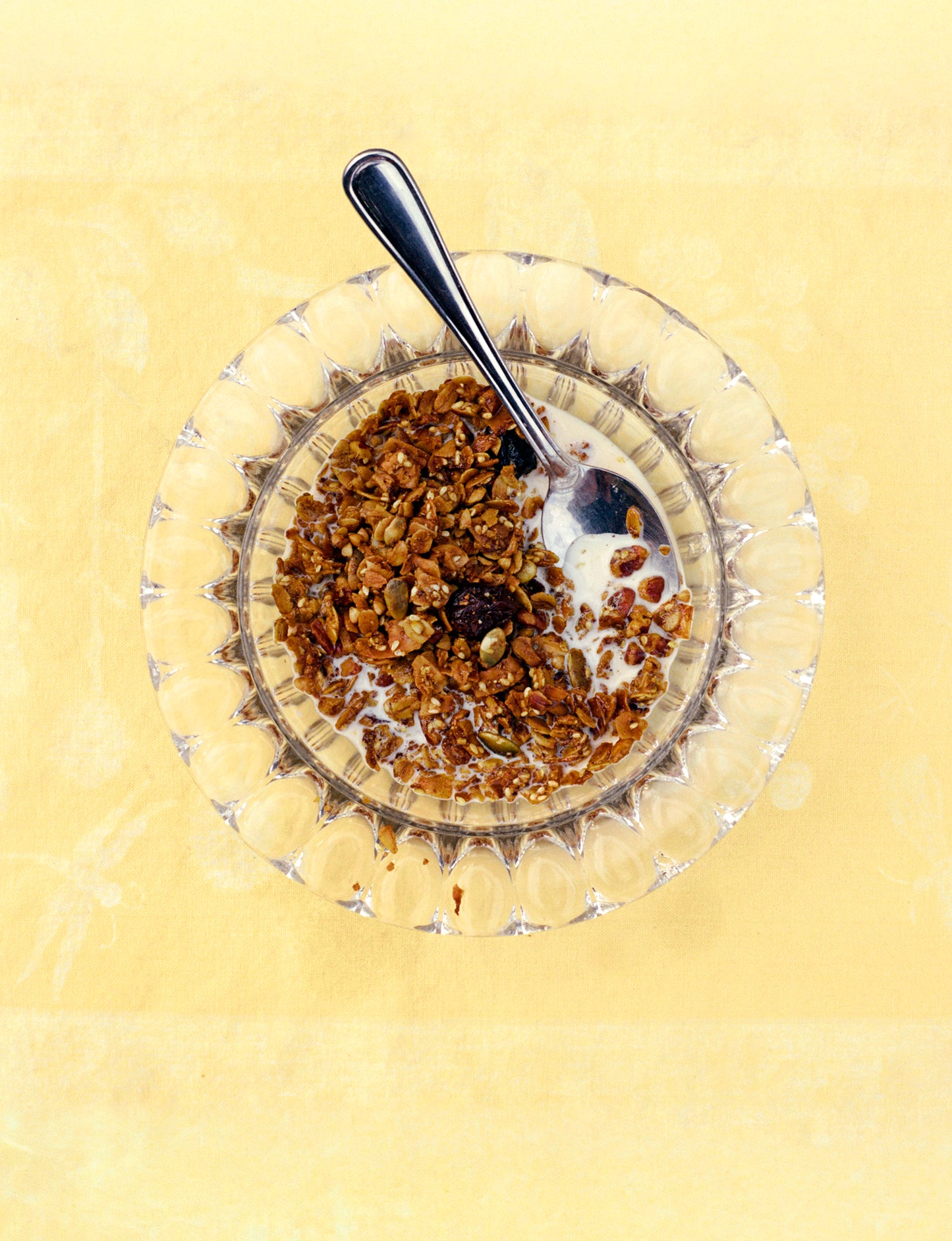 Glass bowl with granola and milk on a yellow background