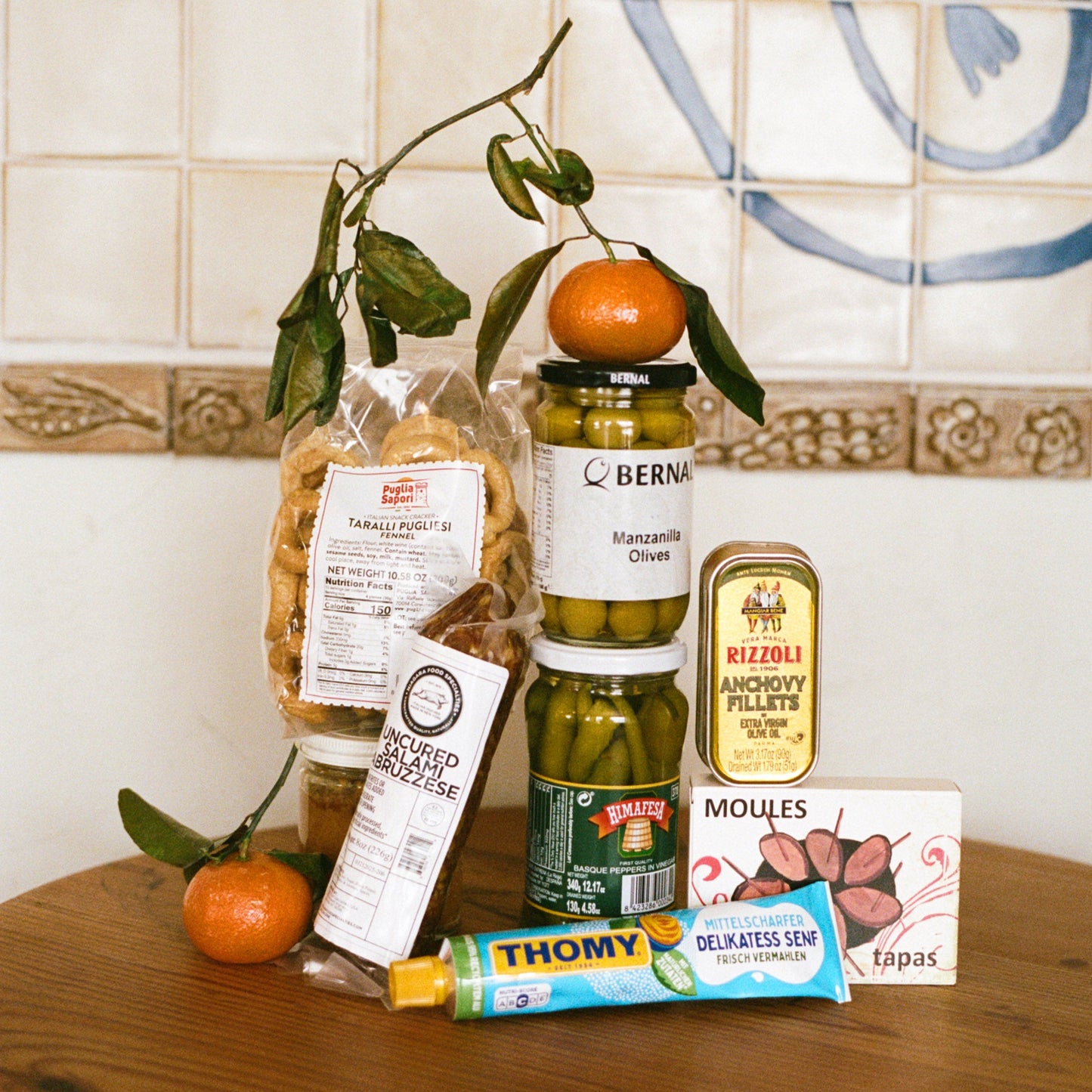 Assorted food products including jars, a box, and a bag on a wooden surface with a tiled wall background.