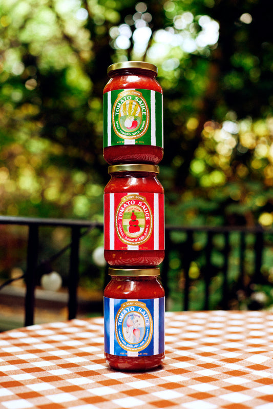 Three jars of tomato sauce stacked on a checkered tablecloth with a blurred green outdoor background