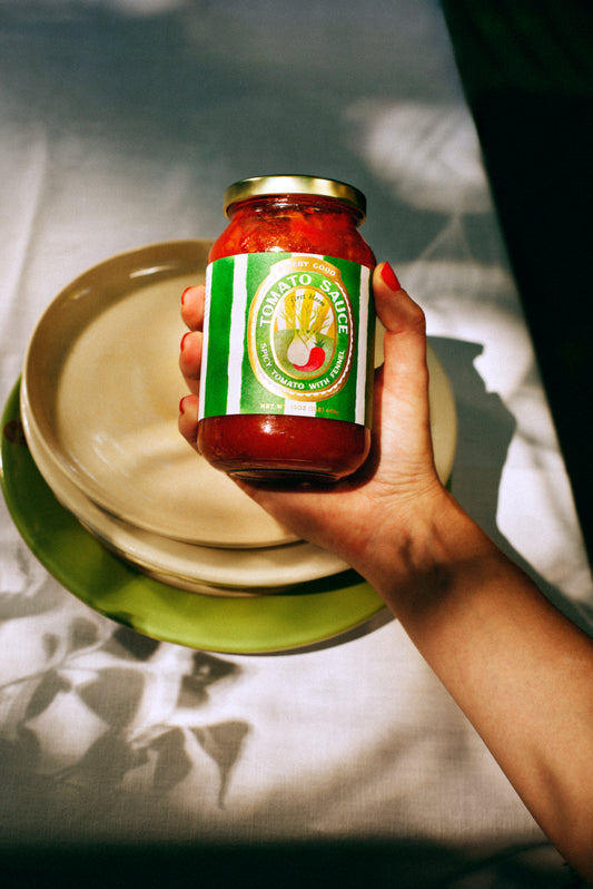 Hand holding a jar of tomato sauce with a green label over a set of plates.