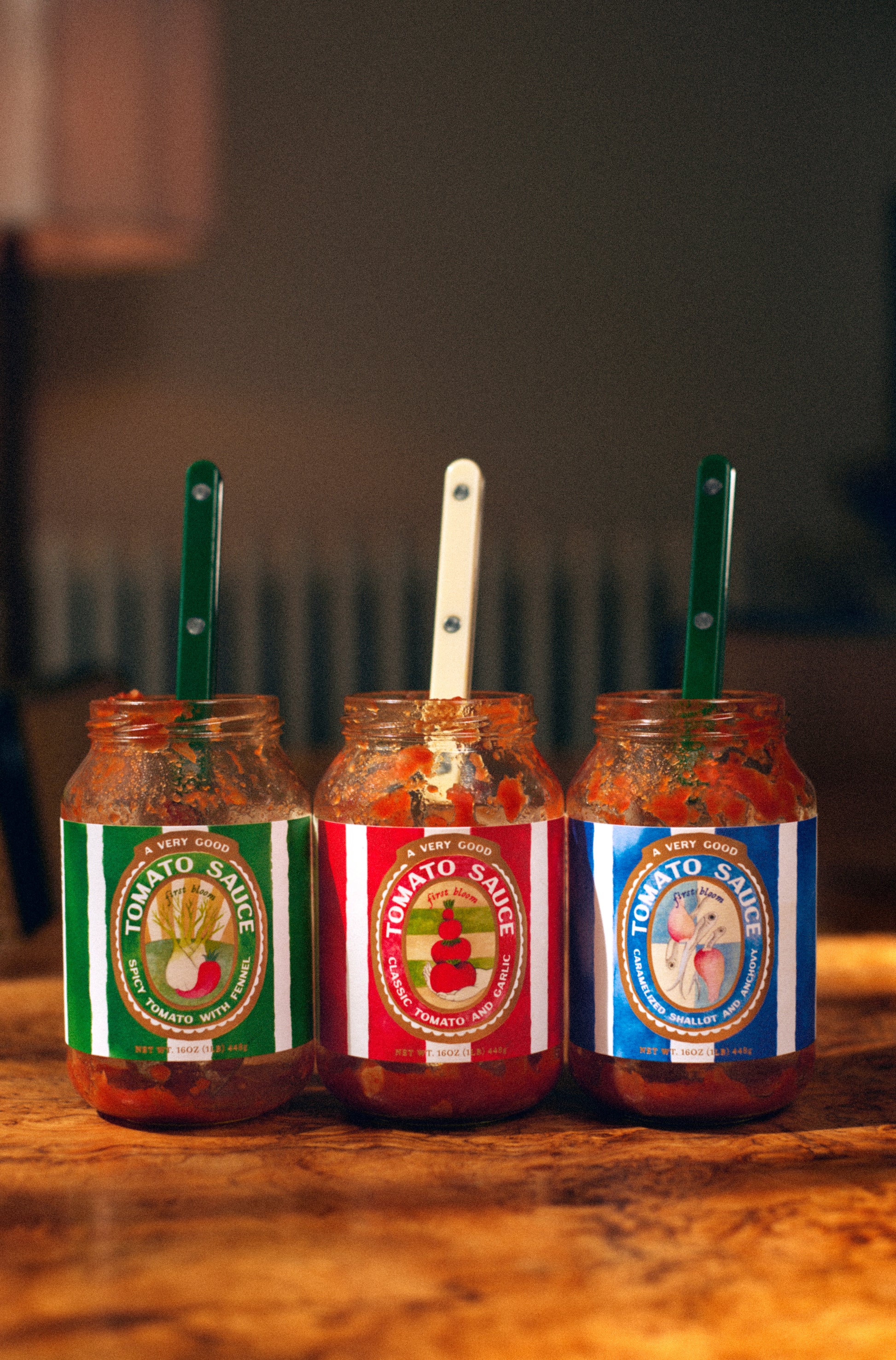 Three jars of tomato sauce with colorful labels on a wooden surface.