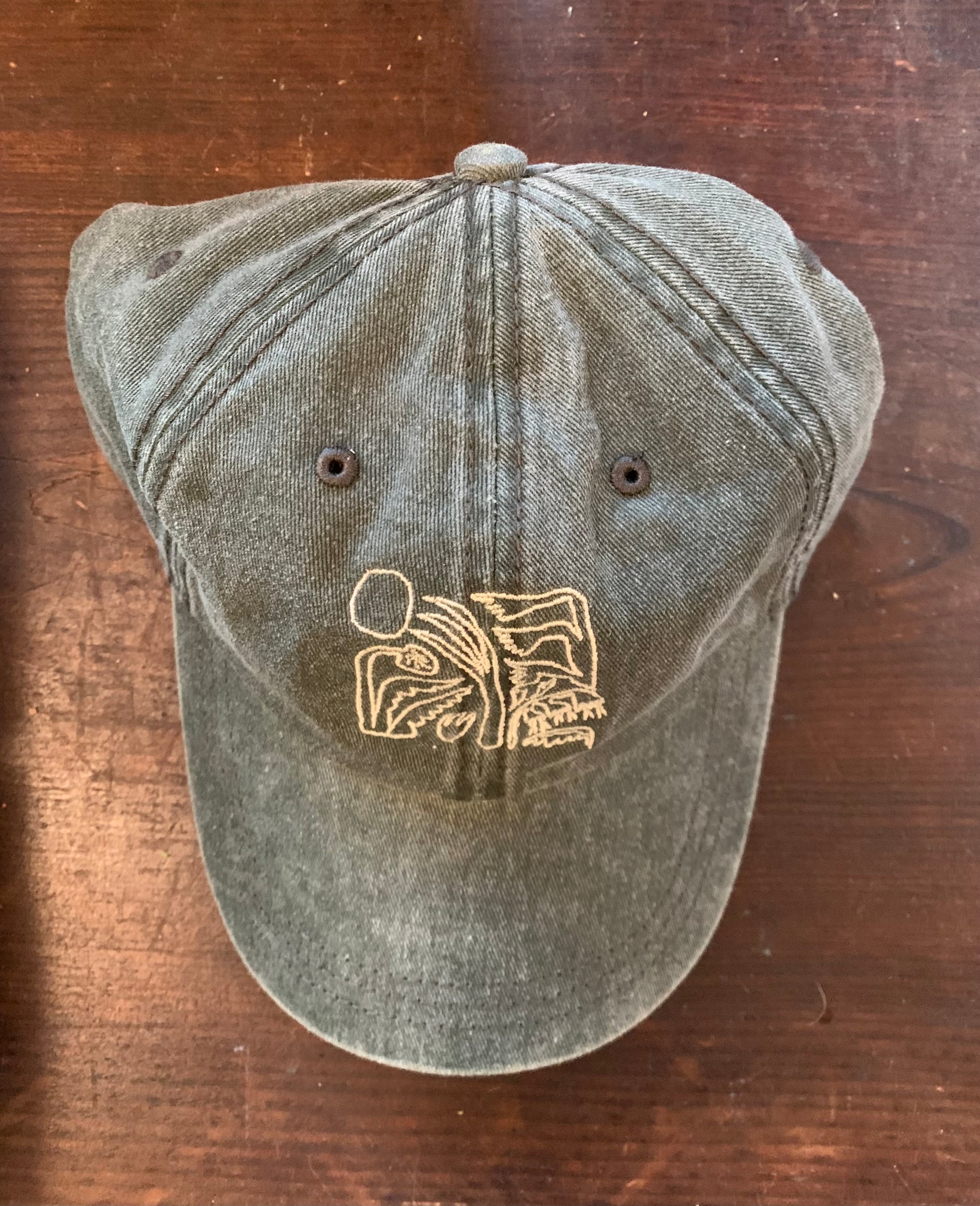 A green baseball hat with an abstract floral design and text on the front, displayed on a wooden surface.
