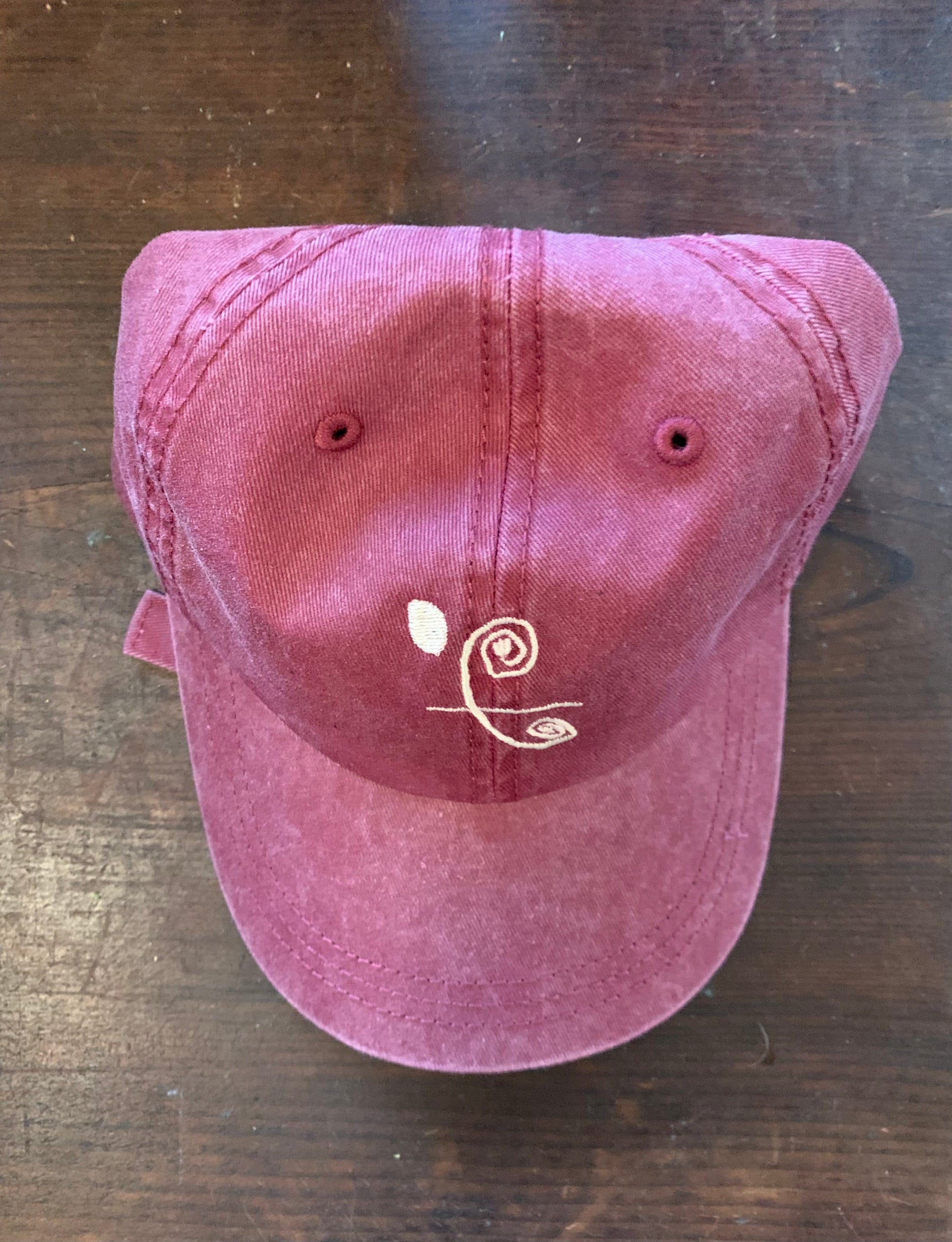 A maroon baseball hat with white text and a logo on the front, displayed on a wooden surface.